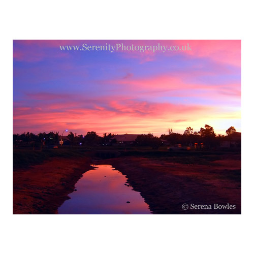 The blue sky over Broome turns pink in the afterglow of sunset, reflected in a strip of water. Western Australia.